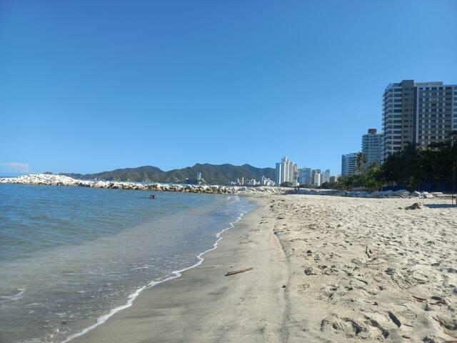 Vista de playa con aguas cristalinas y edificios modernos cerca de apartamentos Premium Suite en Santa Marta
