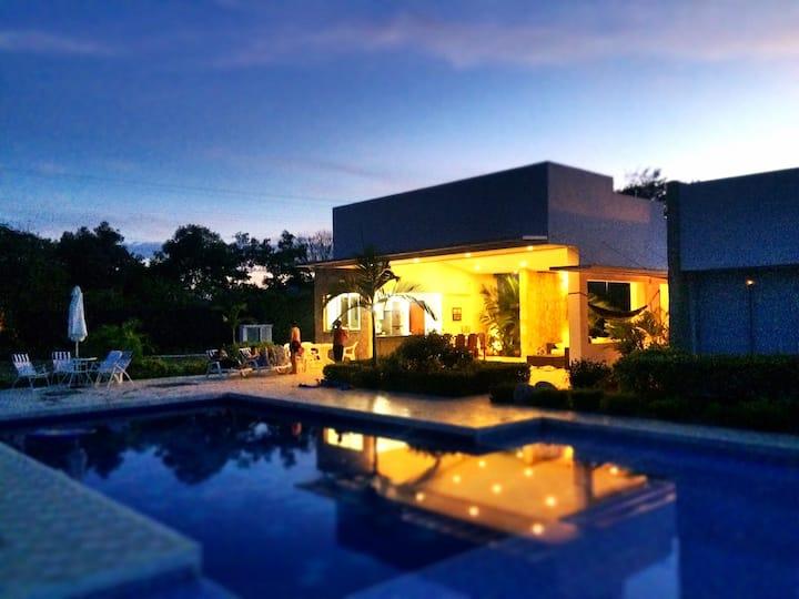 Casa tropical con piscina iluminada al atardecer en Apulo, terraza cubierta con luz cálida