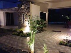 Terraza iluminada de noche en casa tropical con jardín y arquitectura moderna en Apulo