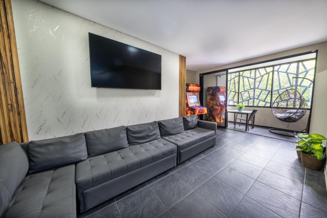 Sala moderna con sofá gris, TV y arcade en apartamento de lujo en Medellín cerca de Lleras