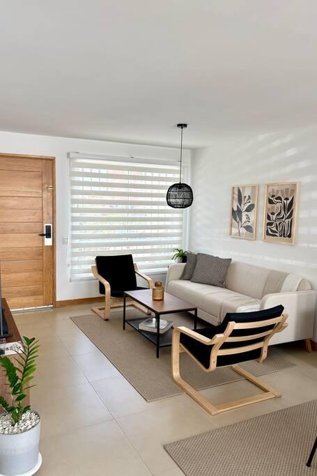 Sala luminosa con sofá beige y sillas de madera en casa vacacional en Rionegro, Antioquia