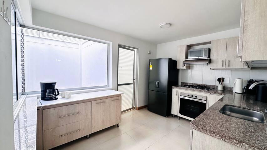 Cocina moderna y equipada de casa vacacional en Rionegro, con refrigerador negro, estufa a gas, microondas y cafetera