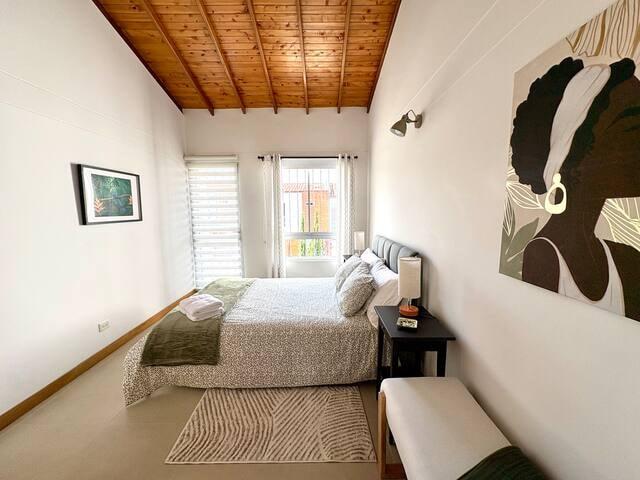 Habitación principal con cama doble, techo de madera y arte decorativo en casa de Rionegro