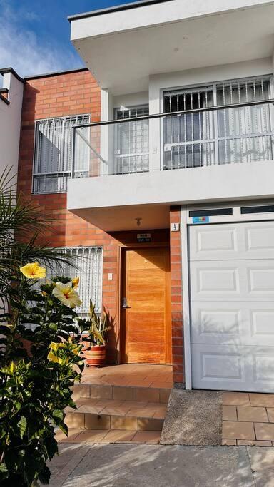 Fachada de casa vacacional en Rionegro con puerta de madera, garaje blanco y balcón en segundo piso