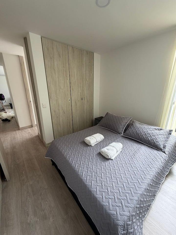Habitación moderna con cama doble, armario de madera y toallas blancas en apartamento elegante Manizales