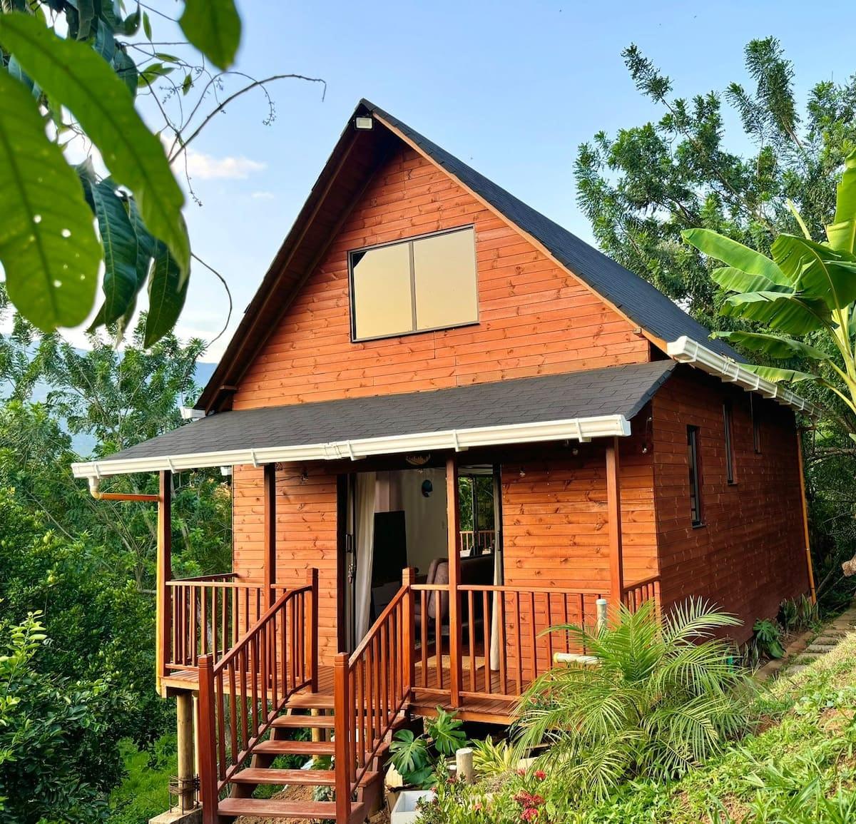 Hermosa cabaña de madera con terraza y escaleras en Girardota rodeada de vegetación tropical
