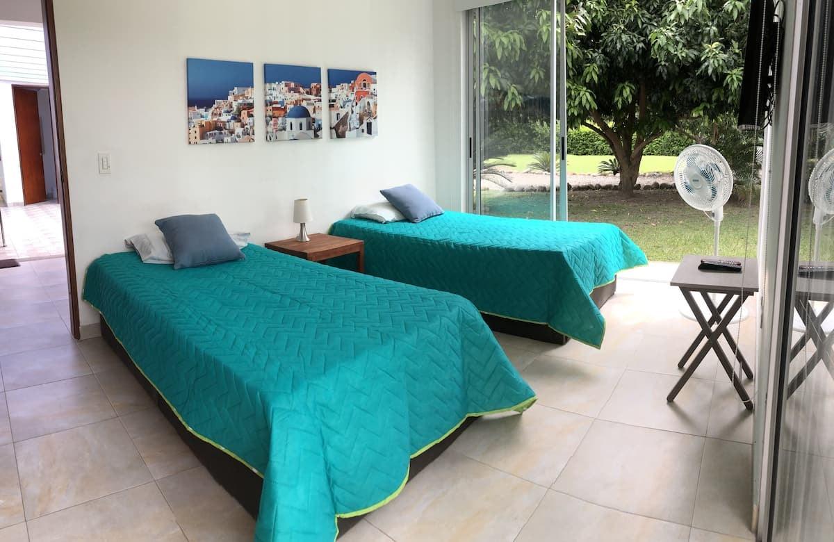 Habitación con dos camas individuales y colchas turquesas en casa tropical de Apulo