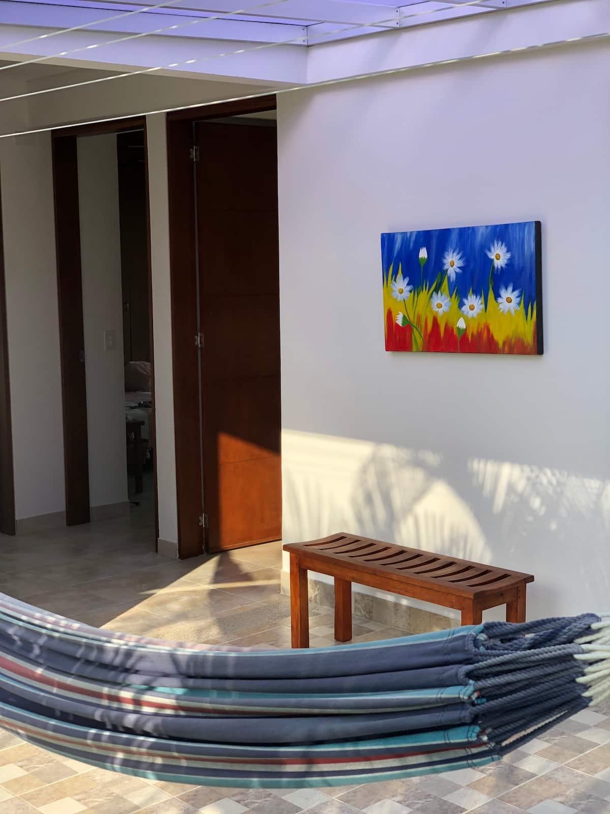 Terraza moderna con hamaca colorida y banco de madera en casa tropical de Apulo