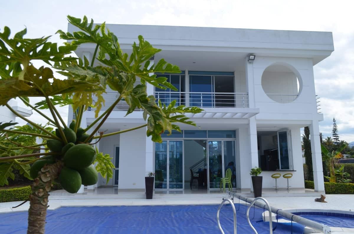 Casa tropical moderna con piscina privada y palmeras en Apulo, fachada blanca con ventanales grandes