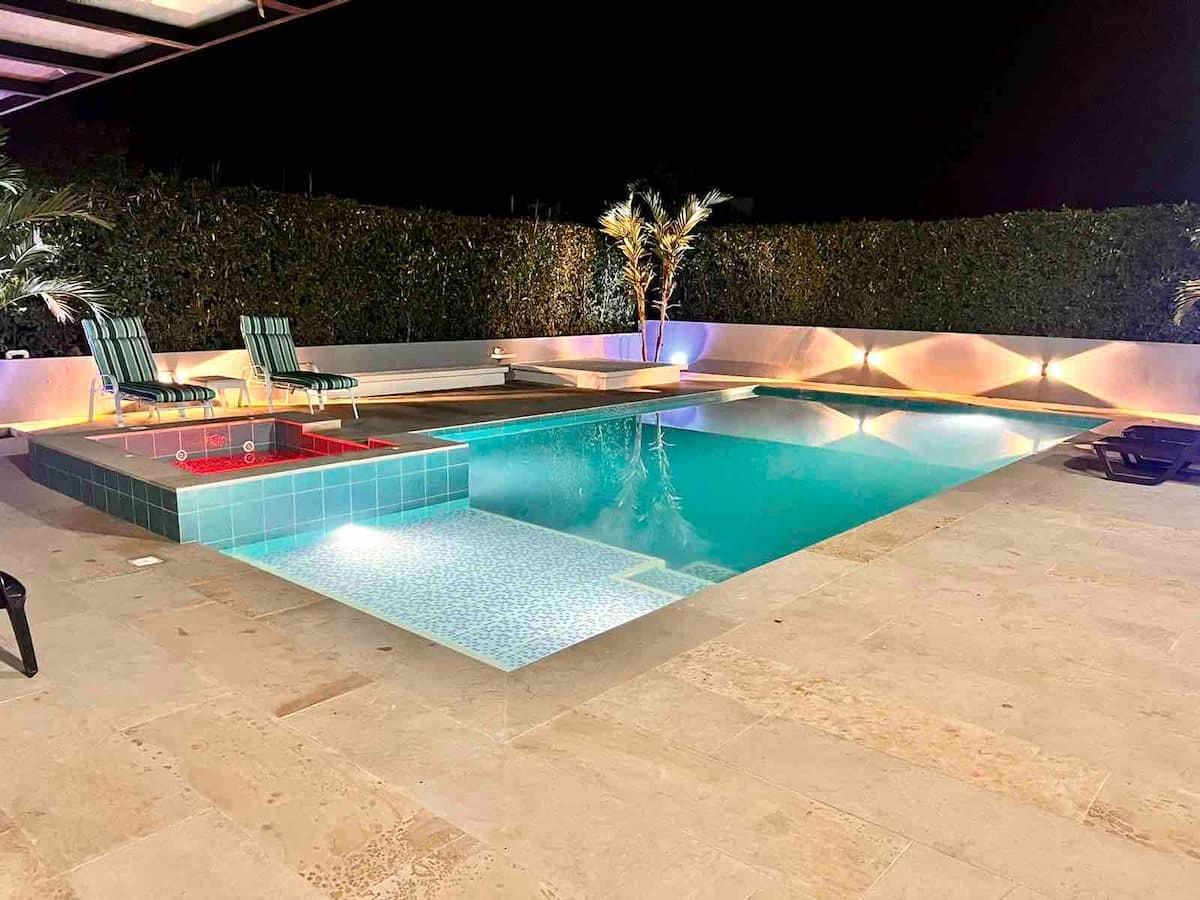 Piscina moderna iluminada con jacuzzi y terraza en casa tropical de Apulo durante la noche
