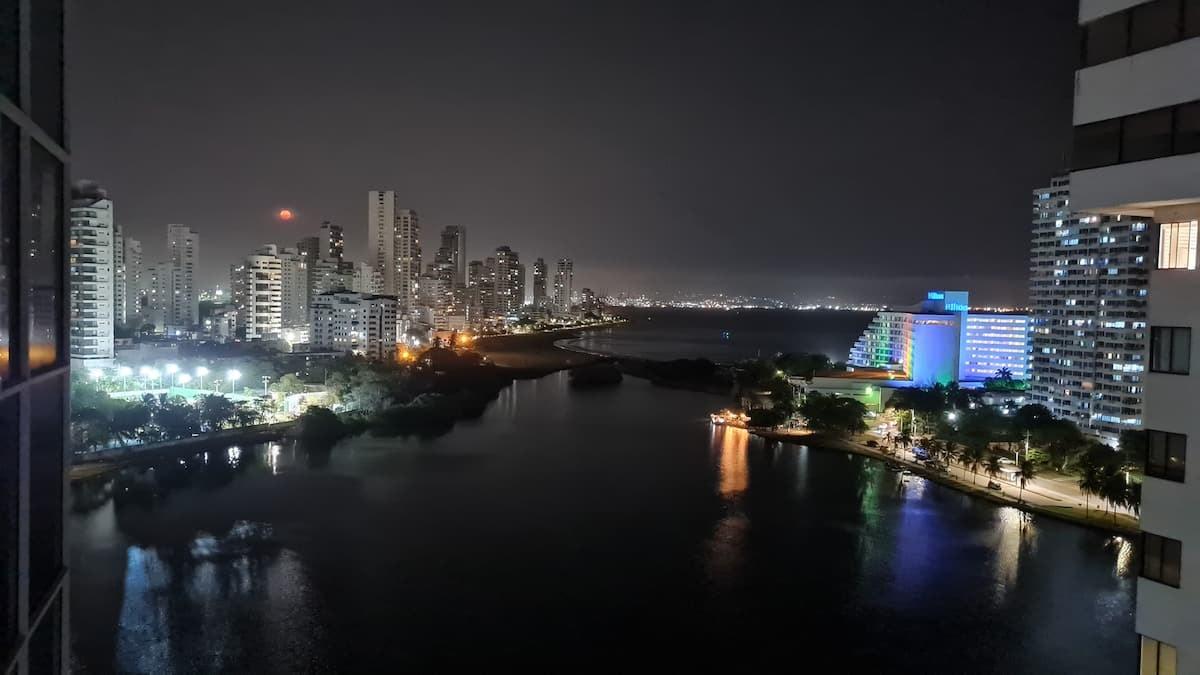 Vista nocturna desde apartamento en Cartagena con ciénaga, edificios iluminados y luces de colores reflejadas