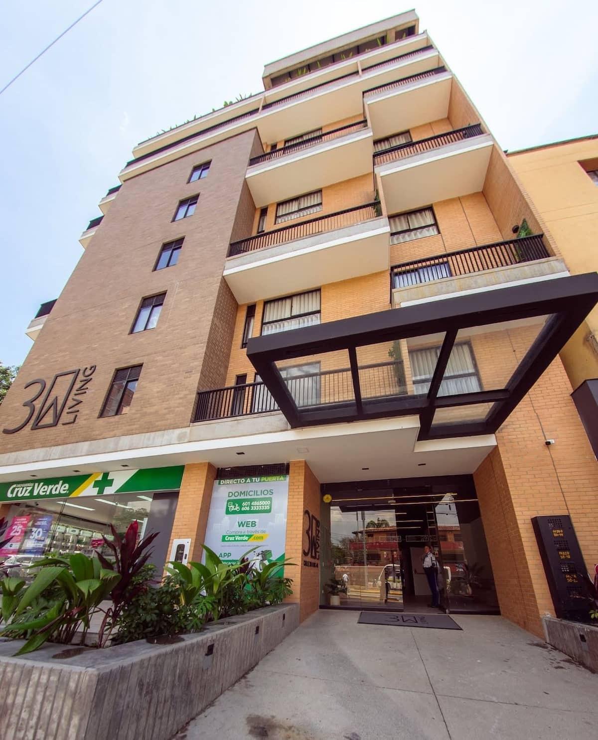 Fachada de edificio moderno con balcones y farmacia en planta baja en Medellín, Colombia