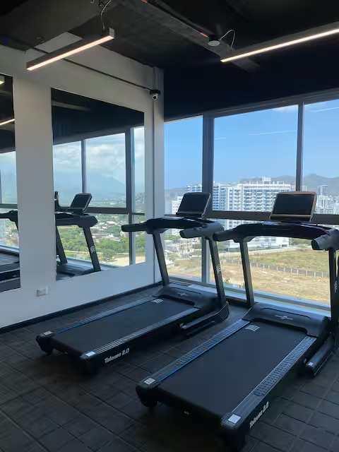 Gimnasio moderno con caminadoras y vista panorámica de la ciudad en apartamento Gaira