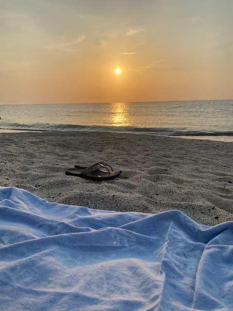 Vista al atardecer desde playa en Gaira con toalla azul y sandalias, apartamento con balcón cercano