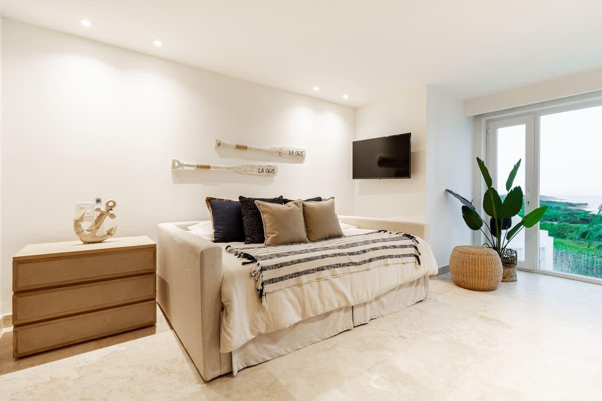 Habitación principal elegante con cama king, TV y vista al jardín en casa de playa Juan de Acosta