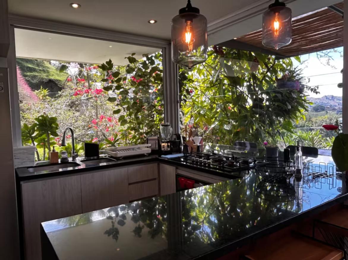 Cocina moderna con encimera negra y ventanales al jardín en villa de lujo en Guatapé