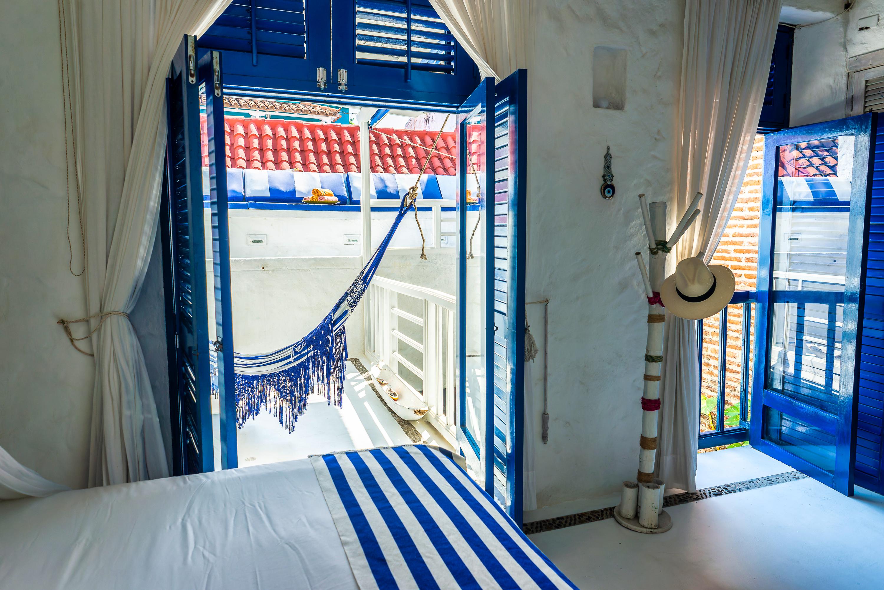 Habitación con cama doble, hamaca azul en balcón y vista a tejados rojos en casa privada Cartagena