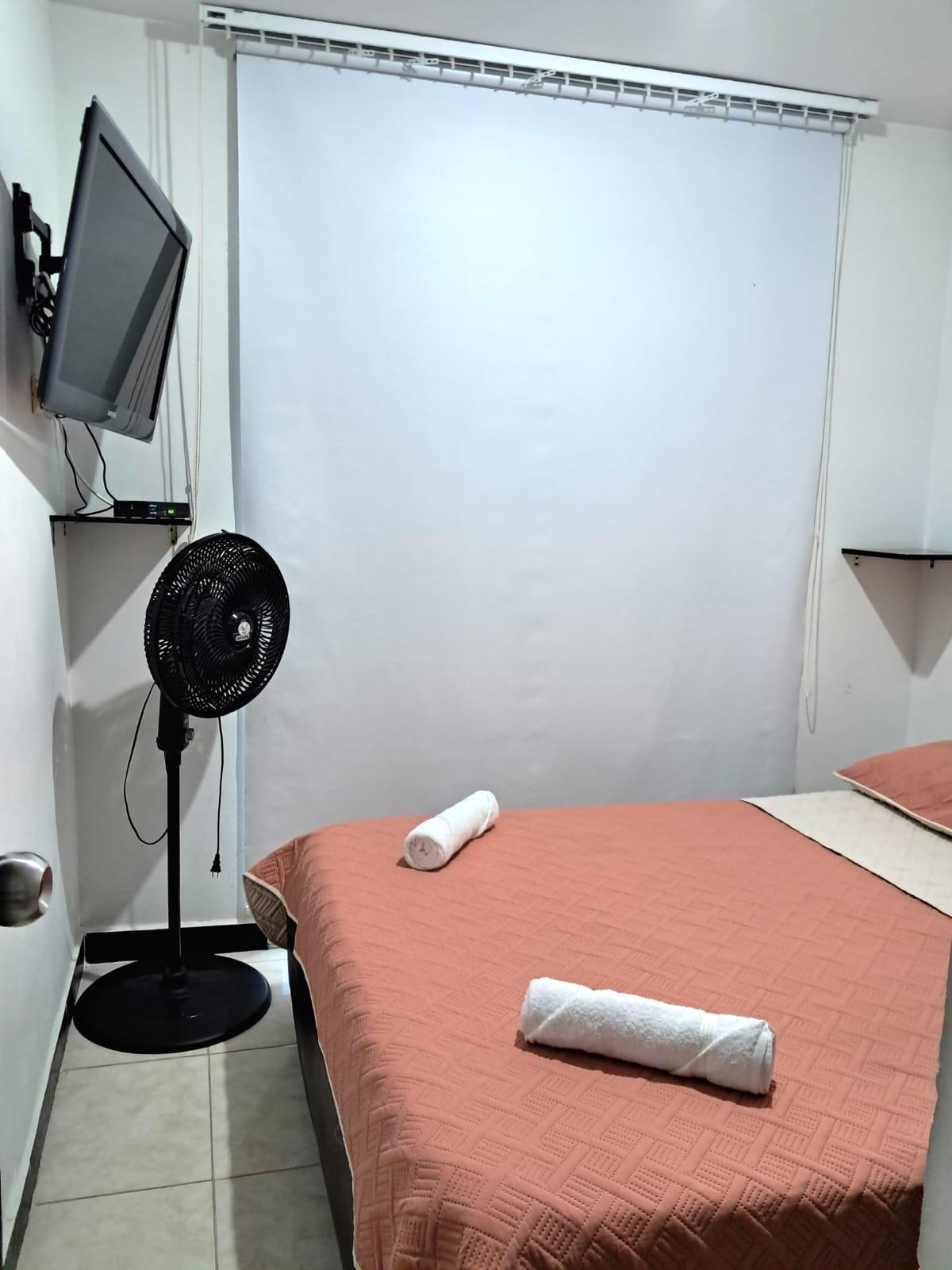 Habitación con cama doble, ventilador, TV y cortinas blancas en apartamento Montenegro